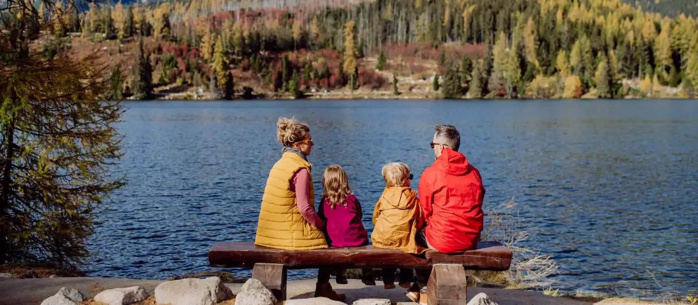 Familie sitzt gemeinsam auf einer Bank und blickt über einen See.