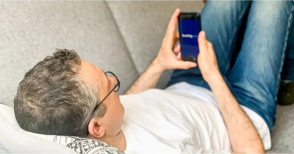 Mann betrachtet auf seinem Smartphone die geöffnete Booking.com-App.
