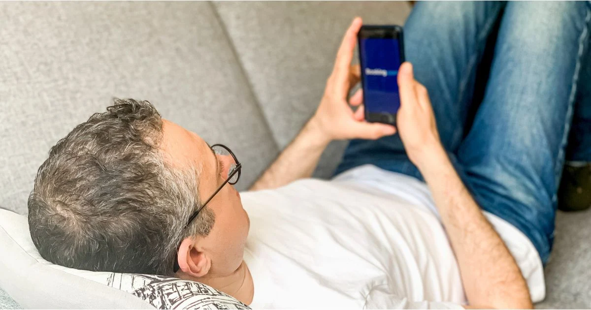 Mann betrachtet auf seinem Smartphone die geöffnete Booking.com-App.