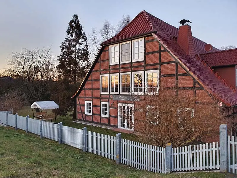 Landhaus Elbeflair mit Fachwerkfassade und Garten steht hinter weißem Zaun.