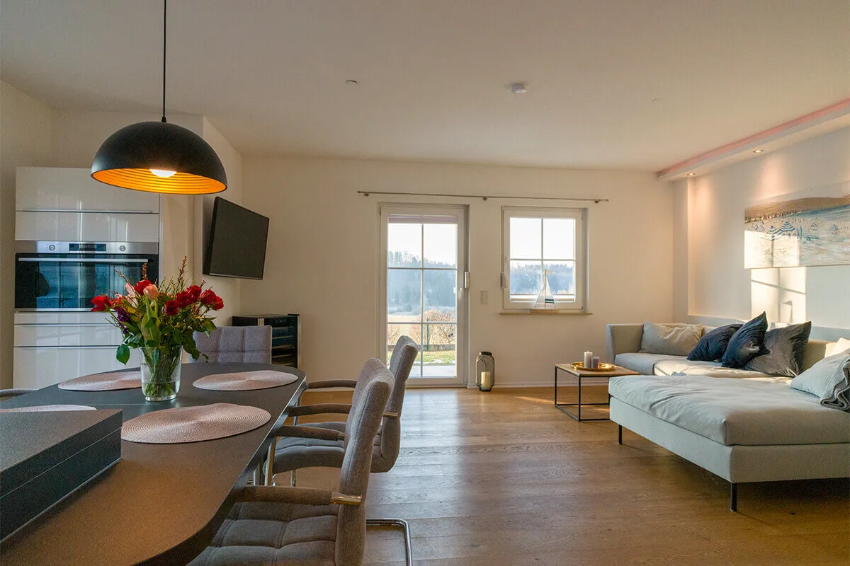 Helle Ferienwohnung mit Wohnbereich, Esstisch, Küche und großer Fensterfront.