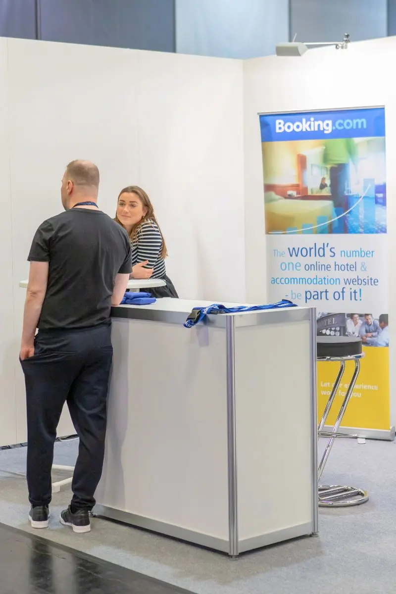 Zwei Personen sprechen an einem Messestand mit großem Booking.com-Banner.