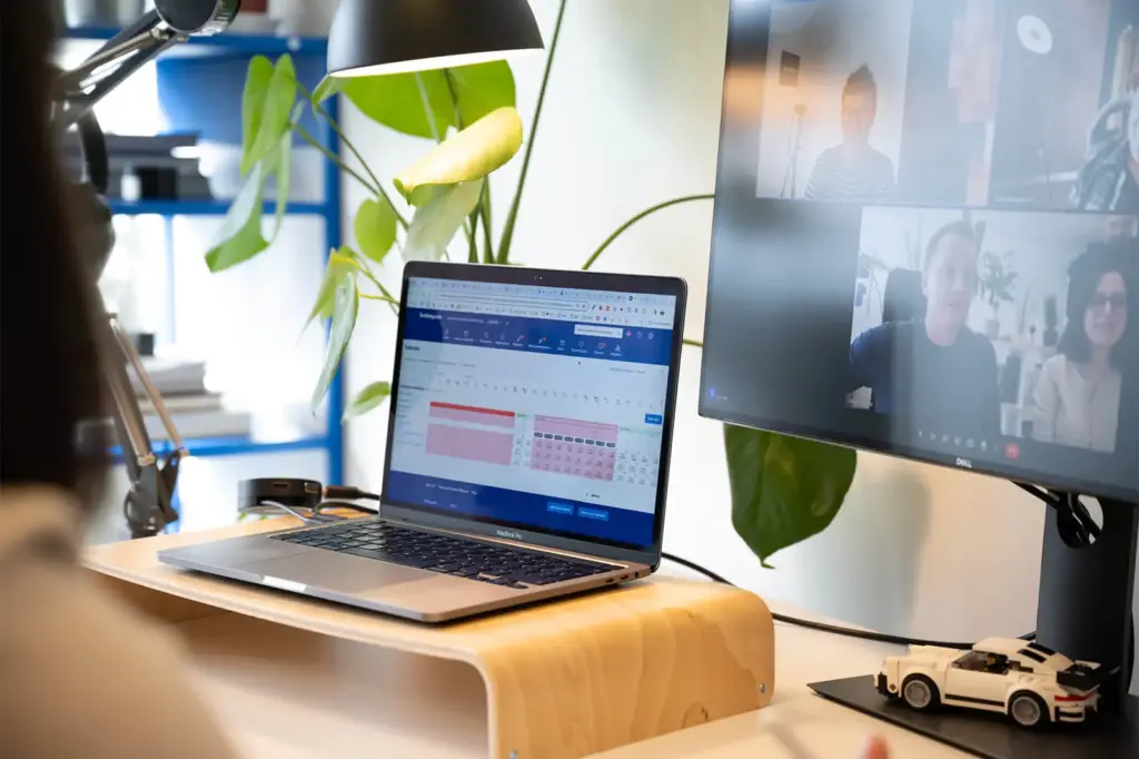 Laptop zeigt Booking.com-Daten neben einem Bildschirm mit laufender Videokonferenz.