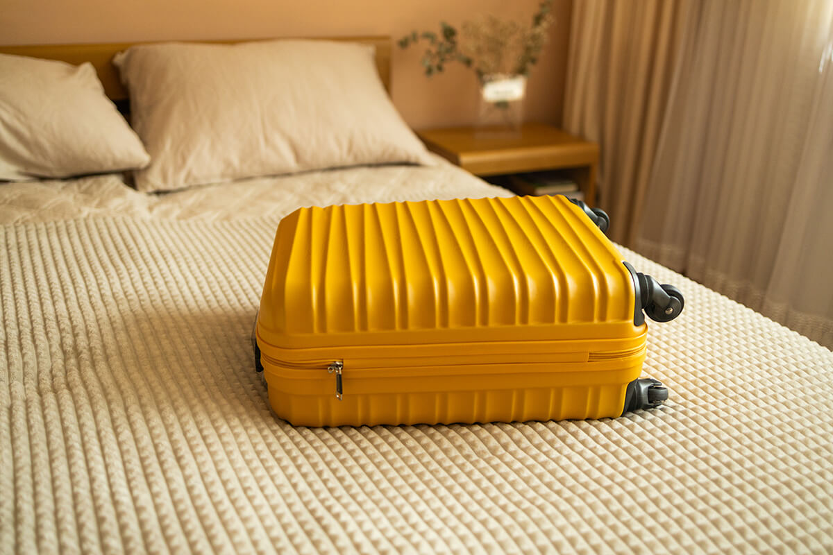 Gelber Koffer auf gemachtem Hotelbett in Ferienwohnung – Symbol für Ankunft, Gastfreundschaft und Reiseerlebnis