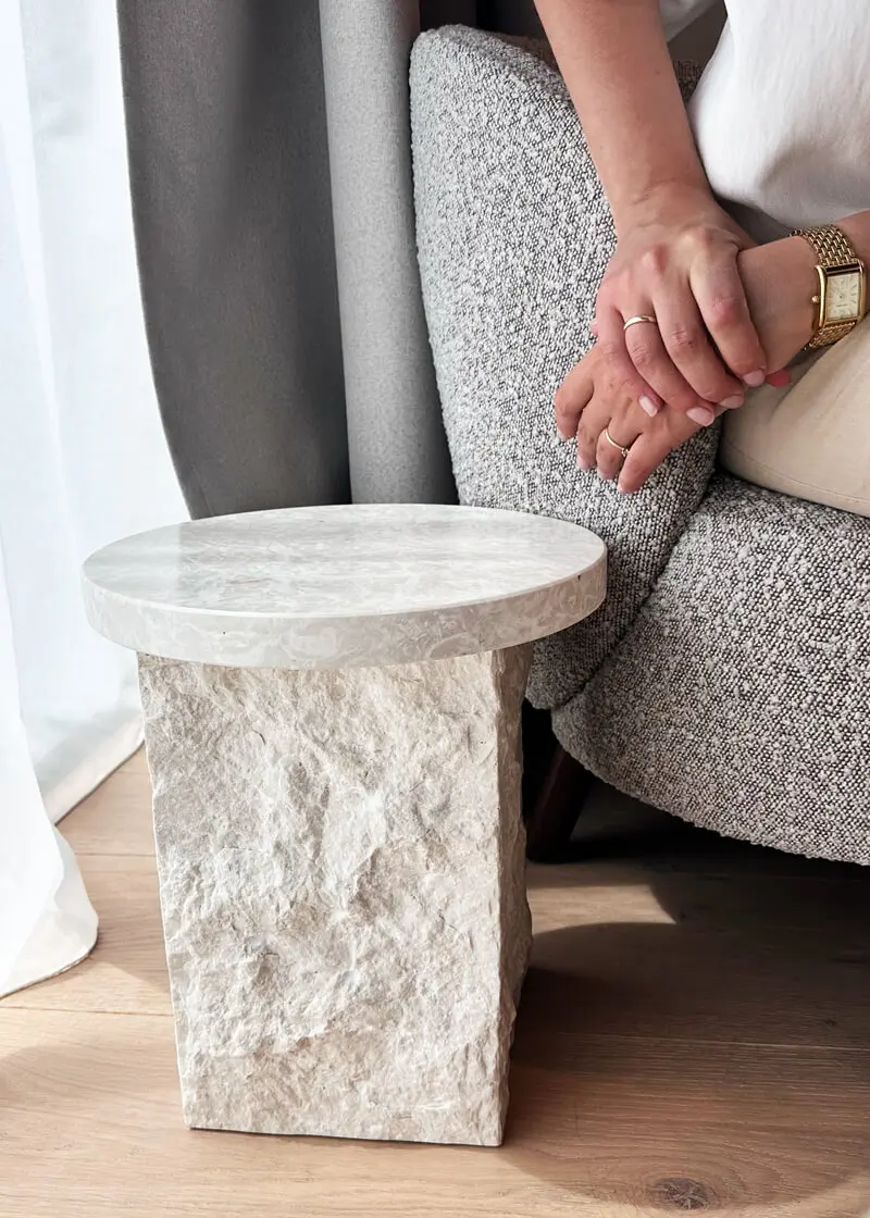 Heller Beistelltisch steht neben einem grauen Sessel mit sitzender Person.
