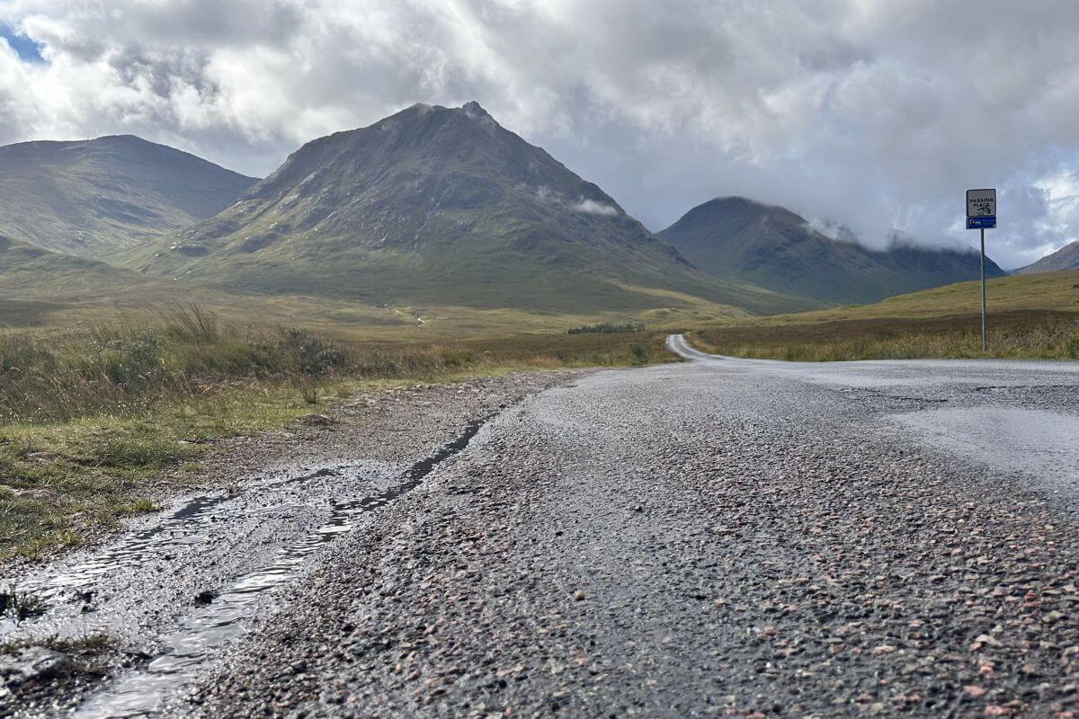 Schmale Straße in den schottischen Highlands mit Bergen und Wolkenstimmung