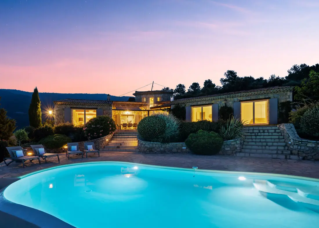 Beleuchtete Villa La Genestière mit großem Pool in südlicher Landschaft.